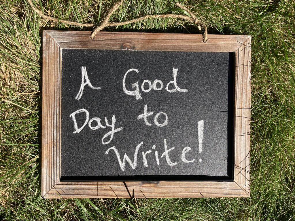 a chalkboard laying in the grass with the message "a good day to write"